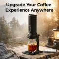 V3 Ständer mit tragbarer Espressomaschine auf einem Campingtisch in der Dämmerung, Eiskaffee im Glas, dahinter eine Laterne