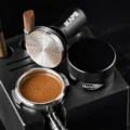 Schwarzer V3 Tamper schräg über einem getampten Siebträger, die Stahlfläche mit Ringen über einem Kaffeebett mit Ringmuster