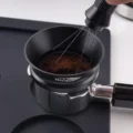 WDT-Nadeln rühren das Kaffeemehl im schwarzen Trichter auf einem Siebträger, auf einer schwarzen Matte
