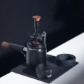 V3 WDT-Tool auf einem Dosiertrichter über einem Siebträger auf schwarzer Matte, daneben der Aufbewahrungssockel