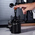 Finger drückt auf den Holzknauf des V3 Tools, das auf einem Trichter über einem Siebträger sitzt