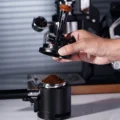 Hand hält das V3 Tool mit angesetztem Trichter über einem Siebträger mit einem Berg Kaffeemehl