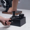 Hand drückt den Tamper in einen Siebträger in der Mulde der Box, daneben steht der Distributor