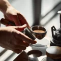 Hand hält den Tamper am Nussbaumgriff neben einem Siebträger mit frisch getamptem Puck mit Ringmuster