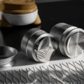Silberner IKAPE Distributor und Tamper liegen seitlich auf der Matte und zeigen die schräge Basis und die Basis mit Ringen