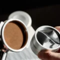 Ebenes Kaffeebett in einem Siebträgersieb neben der Unterseite des silbernen IKAPE Distributors