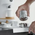 Hand senkt den silbernen IKAPE V4 Palm-Tamper mit der Basis mit Ringen nach unten auf einen Siebträger auf der Matte