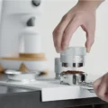 Hand hält den gerändelten silbernen IKAPE Distributor über ein mit Kaffeemehl gefülltes Siebträgersieb