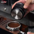 Hand hält den schwarzen V4 mit der Fläche nach unten über einen Siebträger mit geebnetem Kaffee in einer Holzstation