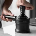 Tampen in einen Siebträger im V4 Ständer, eine Hand auf einem IKAPE Tamper, die andere am Griff