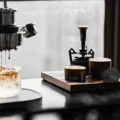 Holztablett an einem hellen Fenster mit dem V4 und anderen Werkzeugen, eine Espressomaschine tropft in ein Glas Milch