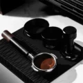 Siebträger mit einem Puck mit Ringmuster auf schwarzer Matte, der V5 steht neben zwei anderen schwarzen Werkzeugen