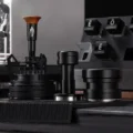 Der V5 auf einer dunklen Matte neben einem IKAPE WDT-Tool und einem Tamper, dahinter unscharf eine Mühle