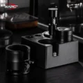V6 in einer schwarzen Tamperstation neben einem Distributor, vorne ein schwarzer zylindrischer Halter, dahinter eine Maschine