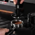 Hand hebt den V6 von einem Siebträger in einer schwarzen Station, im Kaffeebett konzentrische Ringe