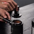 Hände senken den V6 Mini auf einen Siebträger mit Kaffee, der in einem schwarzen Halter auf einem Holztisch steht