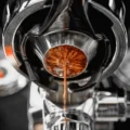 Blick von unten in einen Siebträger mit diesem Sieb, Espresso sammelt sich am schmalen Boden zu einem Strahl