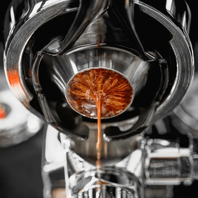 Blick von unten in einen Siebträger mit diesem Sieb, Espresso sammelt sich am schmalen Boden zu einem Strahl