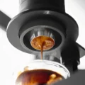 Sieb unter einem schwarzen Brühgerät mit gerändeltem Ring, Espresso läuft aus dem Boden mit 32 mm in ein Glas