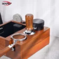 Nussbaum-Tamper in einer Organizer-Box aus Holz neben einem schwarzen Distributor und zwei Puck Screens