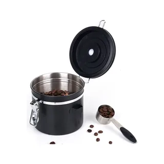 Offene schwarze Dose, teils mit Kaffeebohnen gefüllt, daneben ein Stahllöffel voller Bohnen