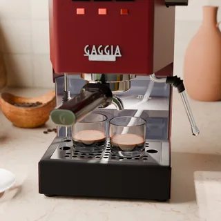 El depósito de agua iluminado de una Gaggia Classic detrás de dos vasos de espresso en una cocina