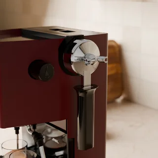 Nahe Ansicht des Siebträgers, der im Halter an einer roten Gaggia Classic in der Küche hängt
