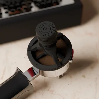 Das Werkzeug von oben auf einem Sieb mit getamptem Kaffee, die Arme über dem Puck